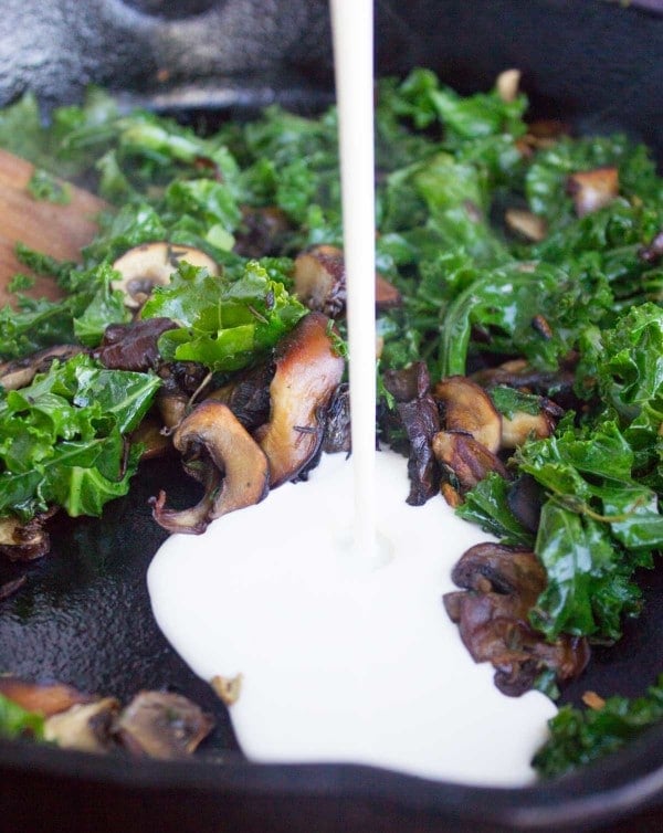 cream being poured into a skillet with fried kale and mushrooms