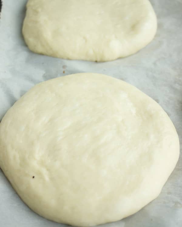 burger buns dough shaped into little circles resting on a baking sheet