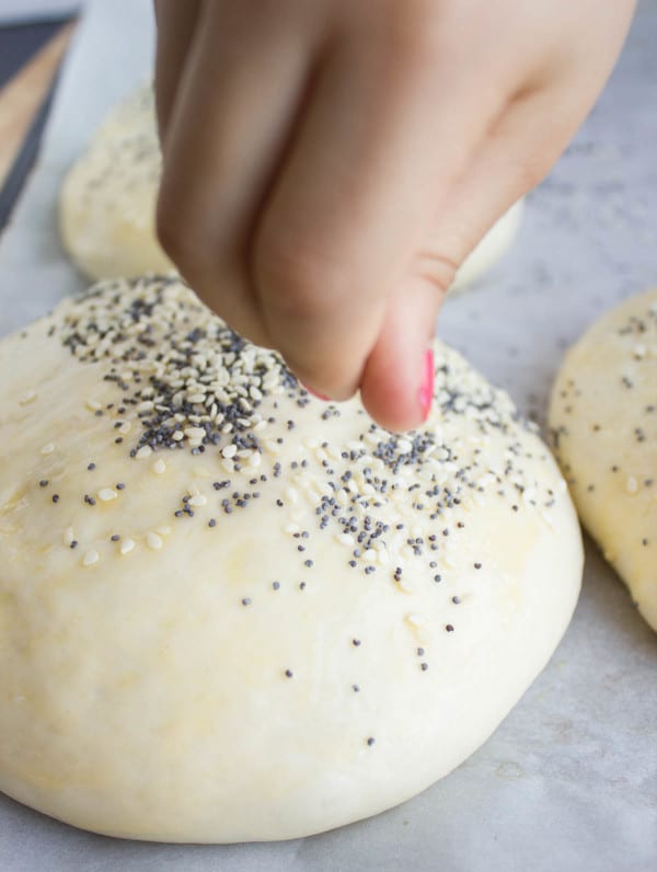 sesame and poppy seeds being sprinkled on a burger bun before baking in the oven