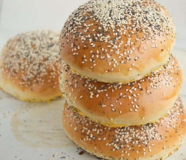 three homemade soft burger buns with sesame and poppy seed topping stacked on top of each other