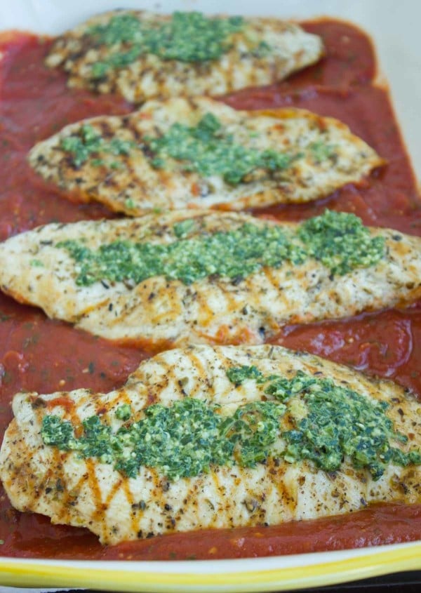 Pollo a la parrilla sobre un lecho de salsa marinara y cubierto con salsa pesto