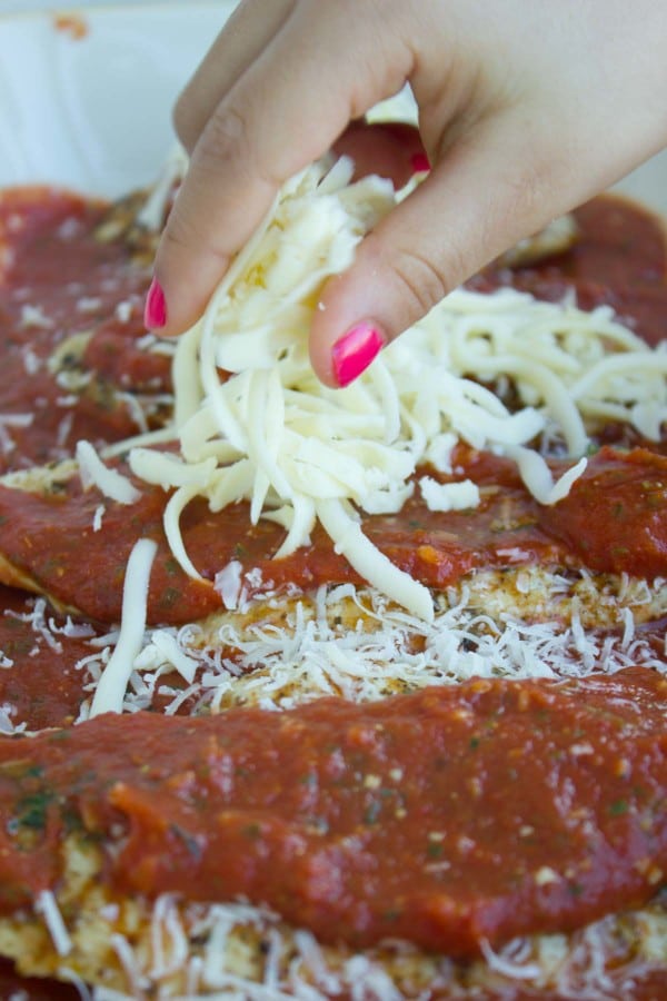 A hand sprinkling more parmesan and mozzarella on top of the chicken breasts and marinara sauce.