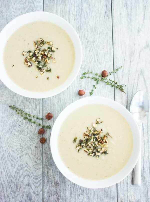 Cauliflower Hazelnut Pear Soup garnished with a crunchy hazelnut topping, served in 2 bowls with some fresh thyme and hazelnuts as decoration
