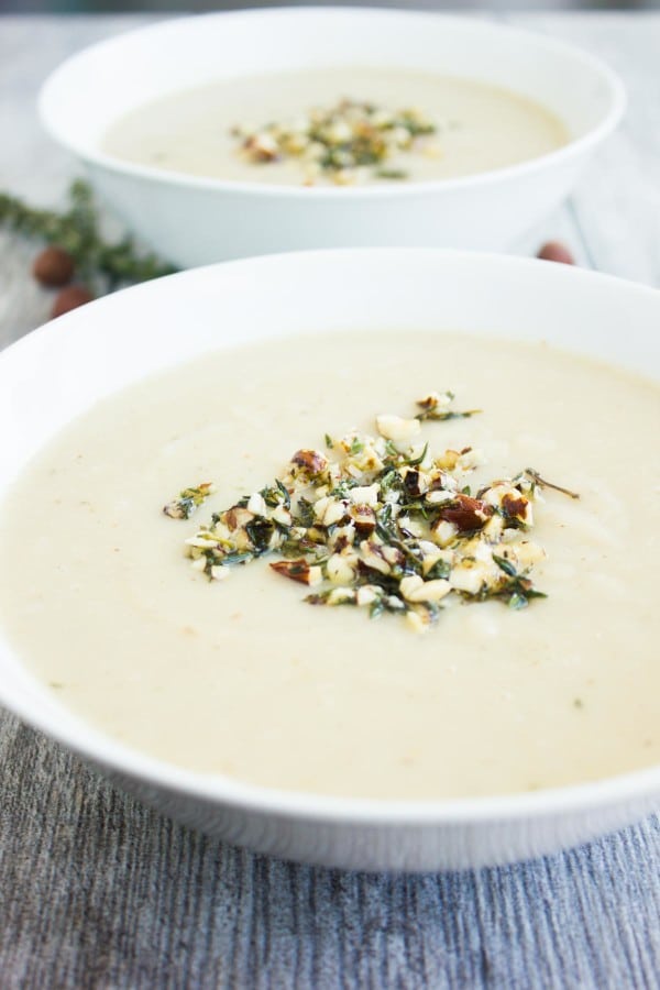 Cauliflower Hazelnut Pear Soup garnished with a crunchy hazelnut topping, served in 2 bowls with some fresh thyme and hazelnuts in the background