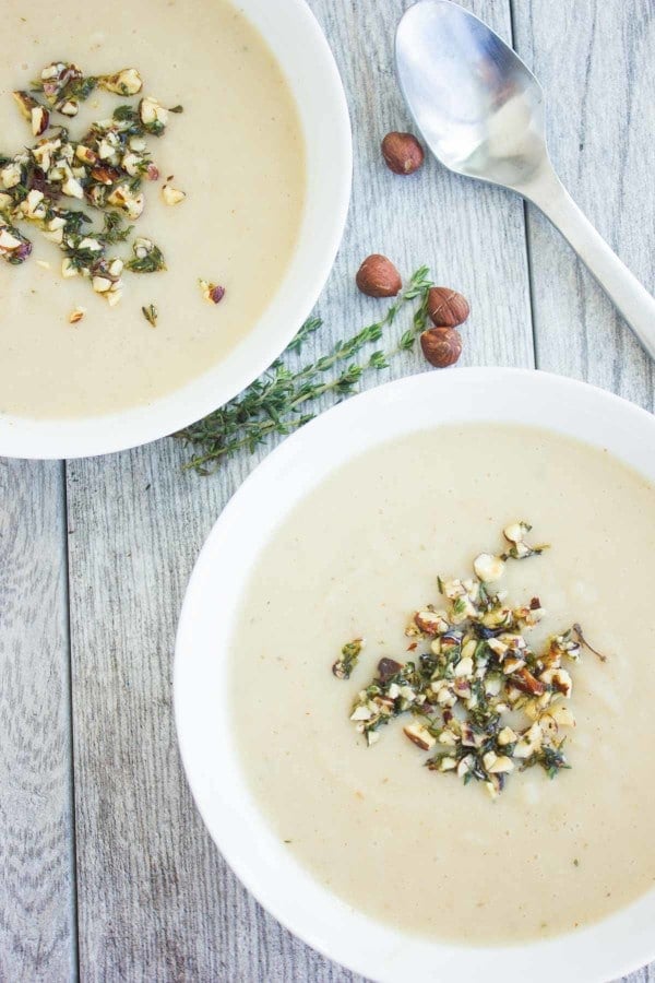 Cauliflower Hazelnut Pear Soup garnished with a crunchy hazelnut topping, served in 2 bowls with some fresh thyme and hazelnuts as decoration