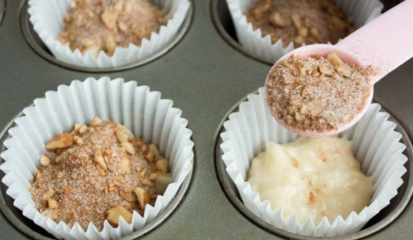 cinnamon sugar being spooned on top of muffin batter in paper cups