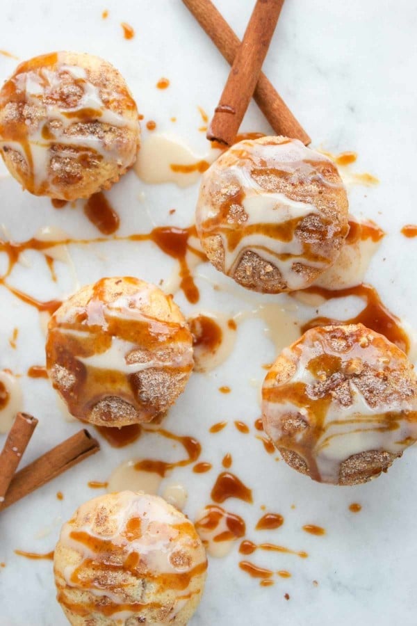 overhead shot of Cinnamon Rolls Muffins on a white countertop with caramel and cream cheese icing drizzled on top