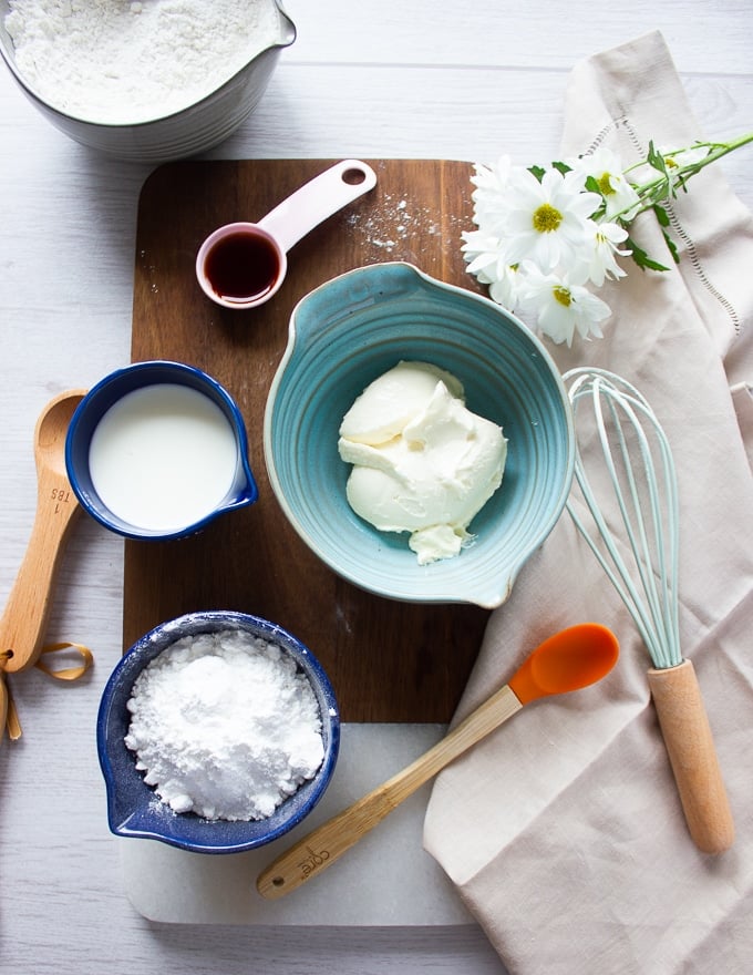 ingredients for cream cheese icing including cream cheese, confectioner sugar, vanilla and milk in separate bowls
