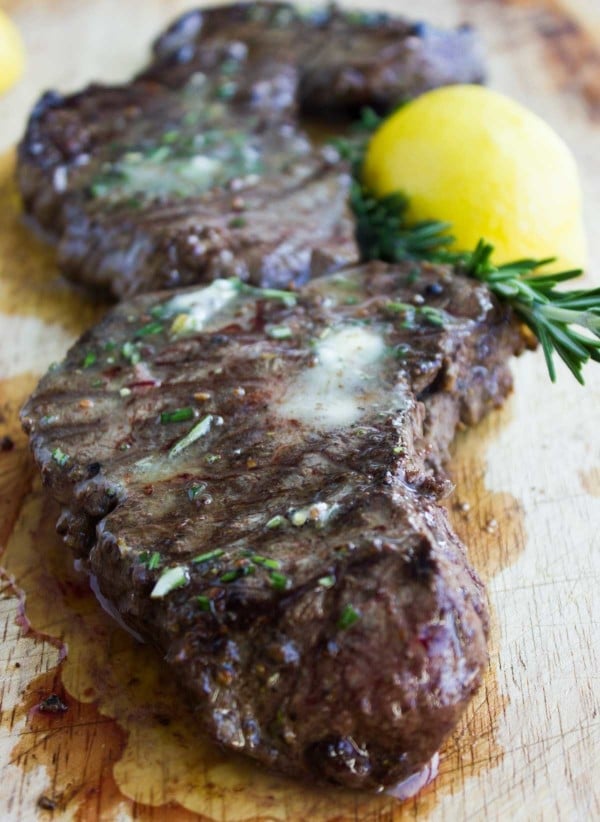 Grilled Steaks with Rosemary Lemon Butter on a wooden chopping board with a lemon and some fresh rosemary in the background