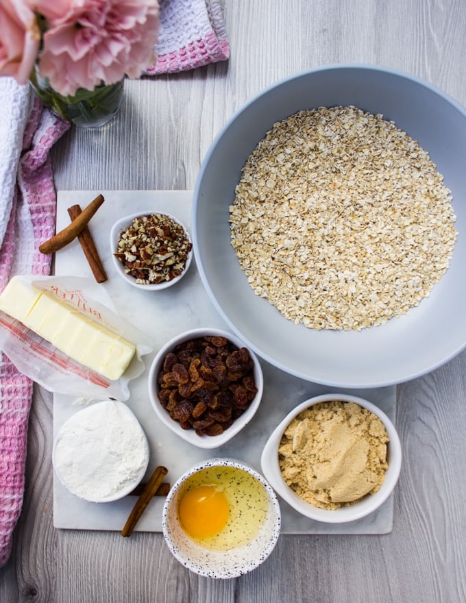 Ingredients for healthy oatmeal cookies: a bowl of oats, bowl of flour, butter, sugars, nuts, raisin, egg and cinnamon