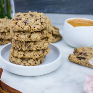 a plate stacked with healthy oatmeal cookies, an expresso cup and cinnamon sticks on a white marble