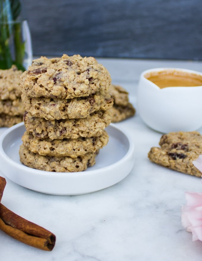 a plate stacked with healthy oatmeal cookies, an expresso cup and cinnamon sticks on a white marble 