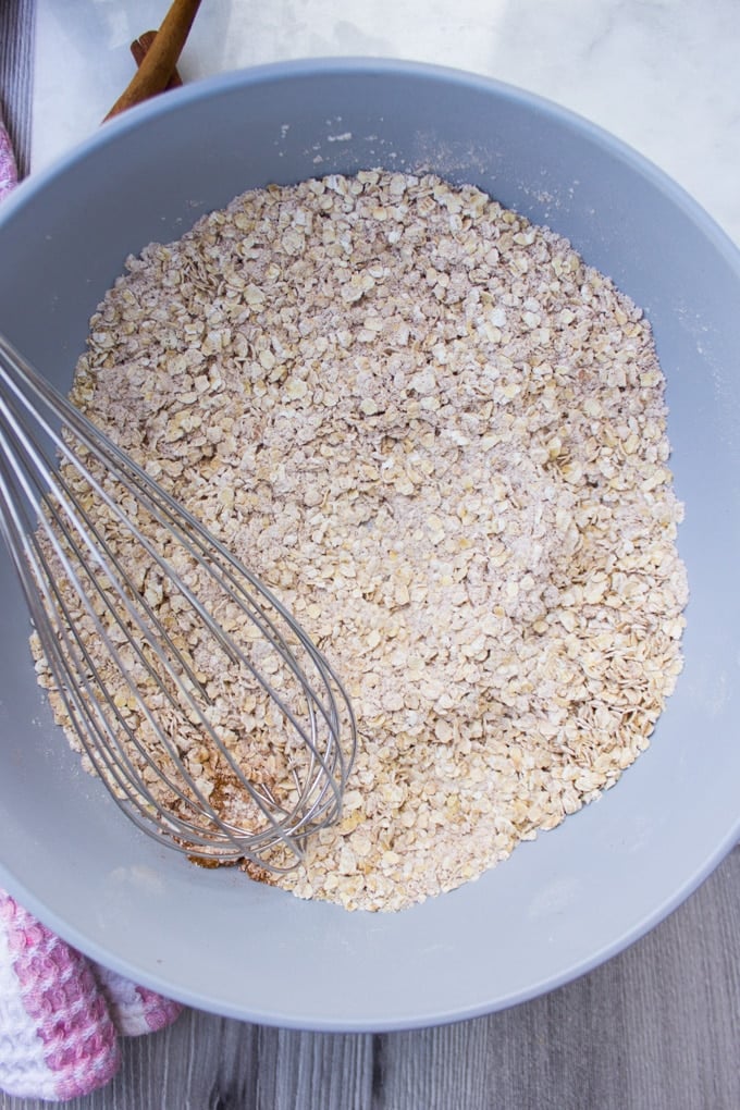 A bowl with oats and flour and whisk to whisk the dry ingredients for the oatmeal cookies