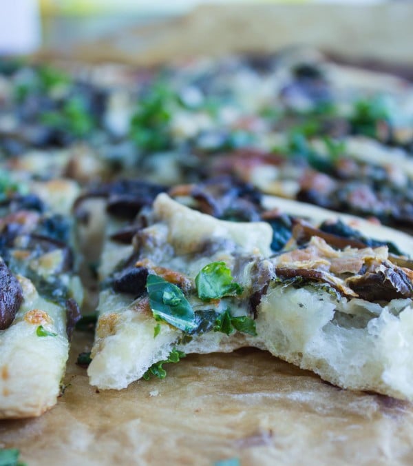close-up of a wedge of kale pizza with mushrooms and brie with one bite missing