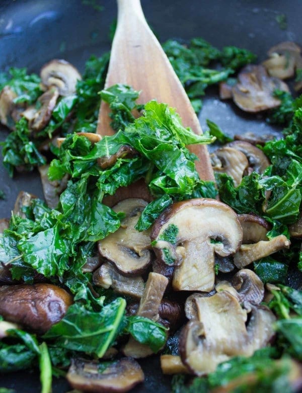 kale and mushrooms being sauteed in a black skillet