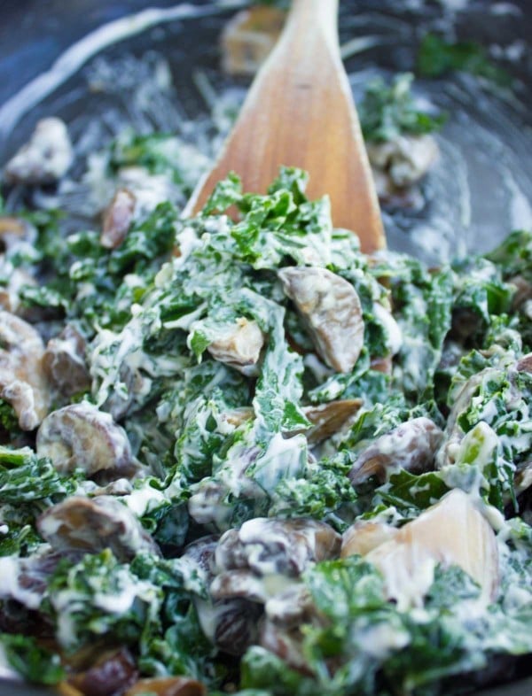 cream cheese being stirred into a skillet with sauteed kale and mushrooms