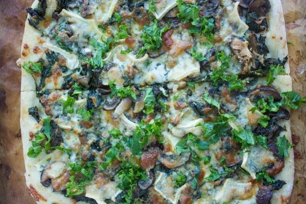 overhead shot of Kale Mushroom Brie Pizza fresh out of the oven on a wooden tabletop