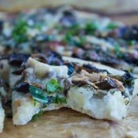 a wedge of Kale Mushroom Brie Pizza with a bite taken out the front
