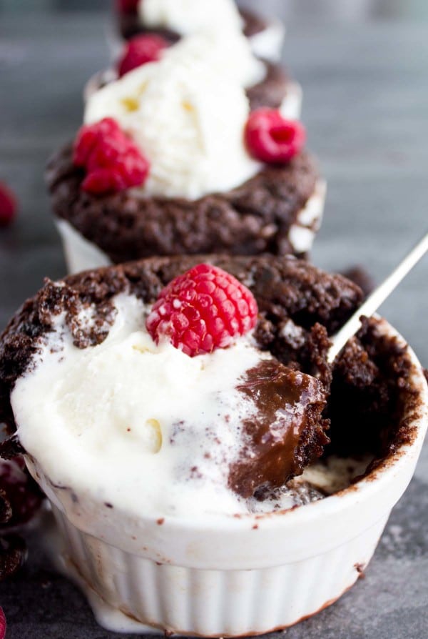 a spoon being dipped into a Mini Chocolate Pudding Cake with half-melted ice cream and fresh raspberries on top
