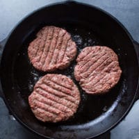 Three burgers on a skillet cooking