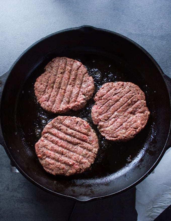 Three burgers on a skillet cooking