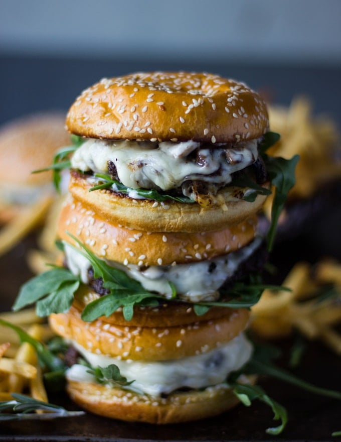 A stack of three mushroom swiss burgers surrounded by french fries