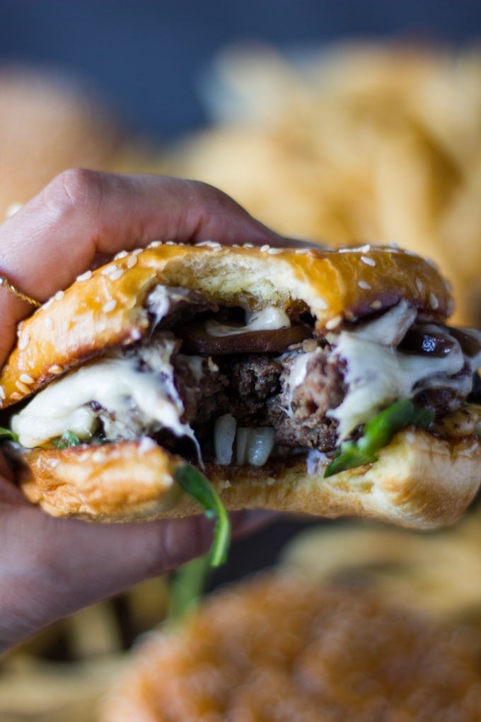 A hand grabbing one mushroom swiss cheese burger bitten up very close up showing the texture of the meat, the mushrooms and melted swiss cheese 