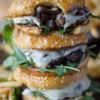 A stack of three mushroom swiss burgers with the top burger bitten up to show the melted swiss cheese, the mushrooms and the burger