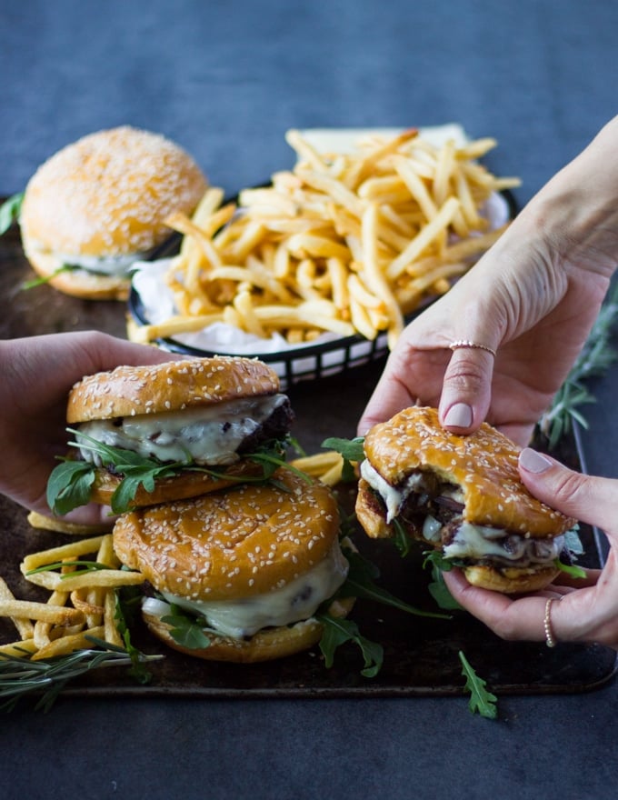 Family hands each picking up a mushroom swiss burger and fries to enjoy the burger meal