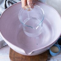 Water is measured into a white mixing bowl with a clear glass measuring cup.