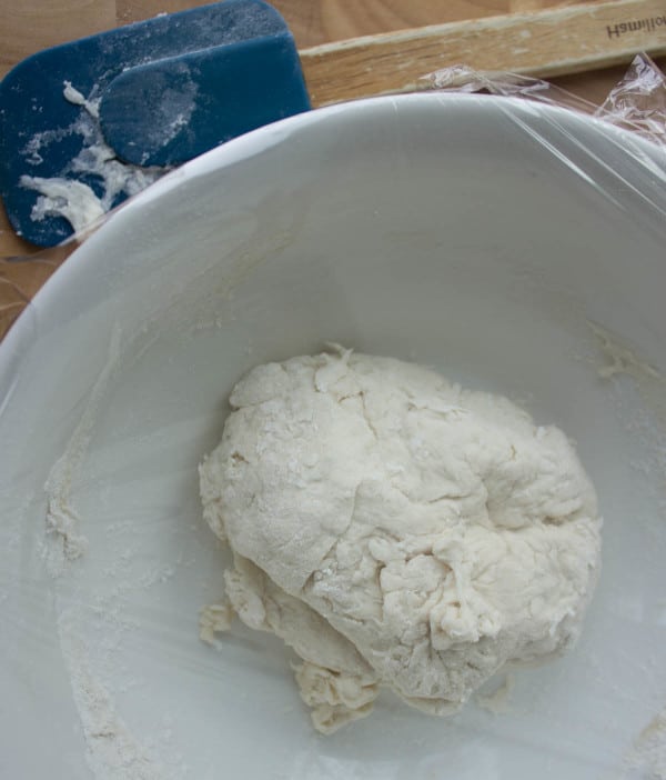 No knead overnight Pizza Dough in a white bowl covered with cling film