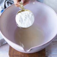 Flour is scooped into a mixing bowl which contains a mixture of water and honey.