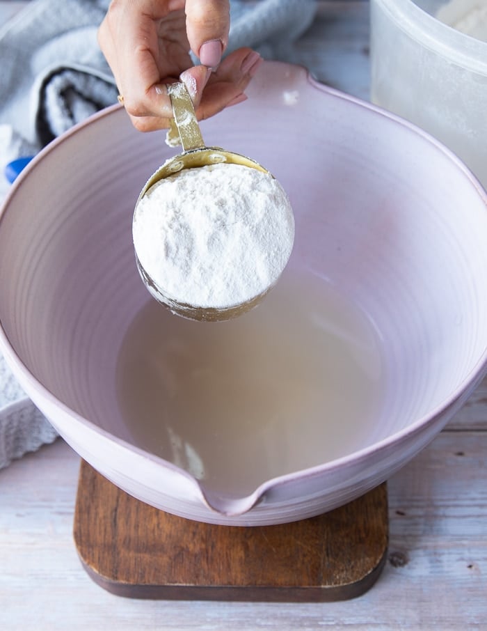 Flour is scooped into a mixing bowl which contains a mixture of water and honey.