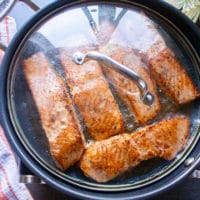 salmon fillets in a skillet flipped and covered with a lid