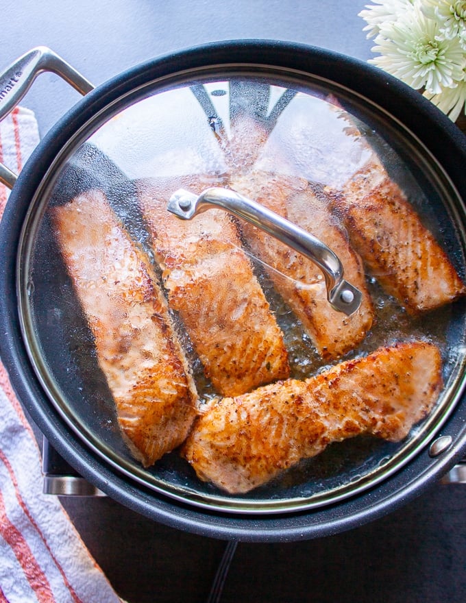 salmon fillets in a skillet flipped and covered with a lid