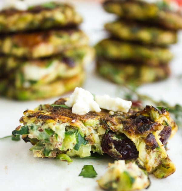 close-up of gluten-free pan-fried zucchini fritter studded with cranberries and feta cheese, with one bite taken out the front