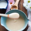 Cream cheese icing in a bowl and a spatula dripping it over the plate showing the smooth consistency