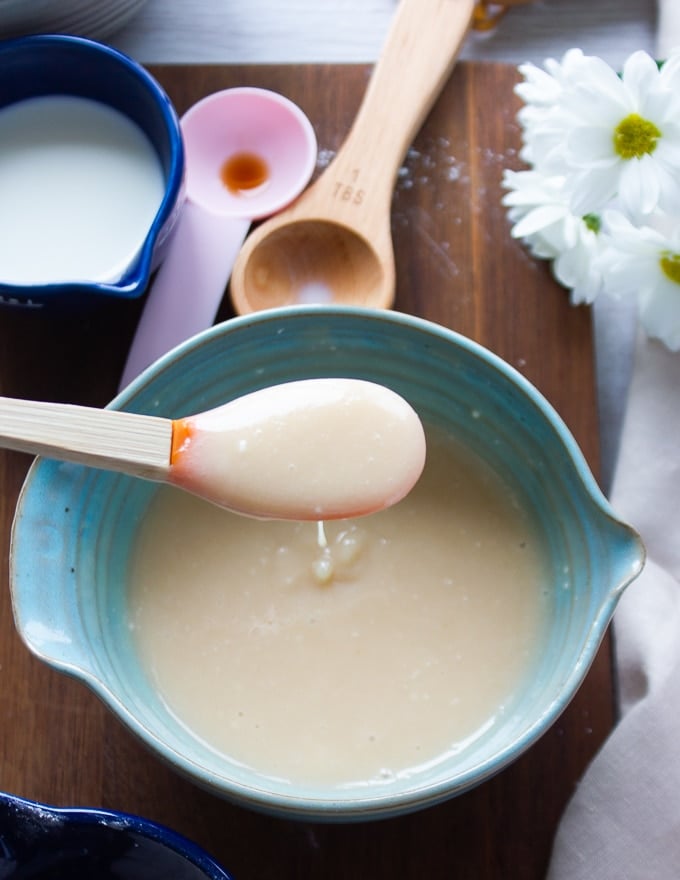 Cream cheese icing in a bowl and a spatula dripping it over the plate showing the smooth consistency  