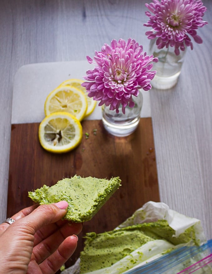 A hand holding a chunk of frozen basil pesto ready to use