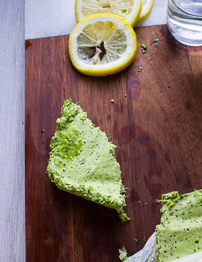 A chunk of frozen basil pesto on a wooden board surrounded by a slice of lemon