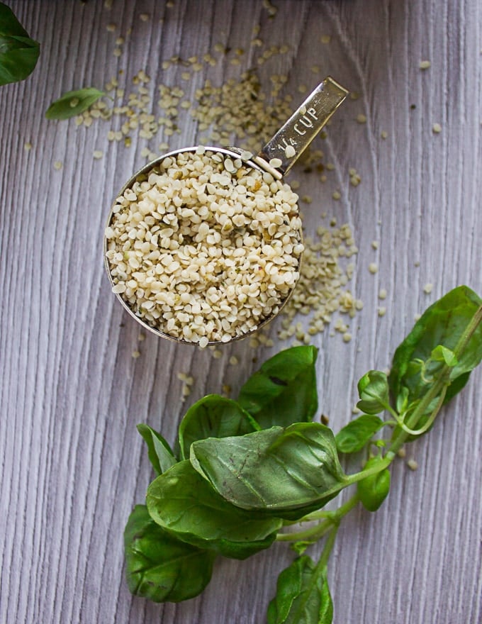 A cup of hemp seeds showing the texture and look of hemp surrounded by fresh basil leaves