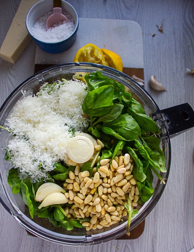 All basil pesto ingredients in a bowl of a food processor ready to make pesto sauce. 