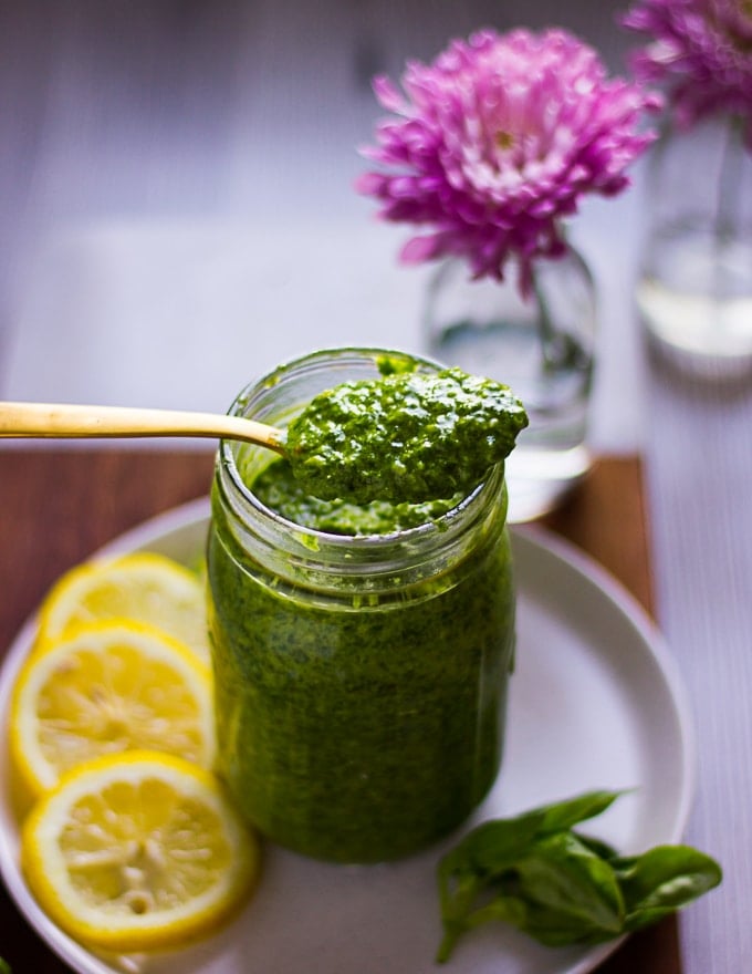A spoon holding a spoonful of basil pesto over a jar of pesto 