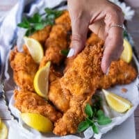 A hand holding a piece of chicken fingers close up showing the texture and crunch of the cooked chicken