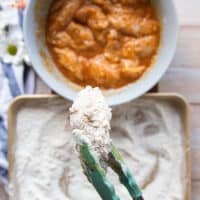 A hand holding a fully coated piece of chicken showing the final flour coating.