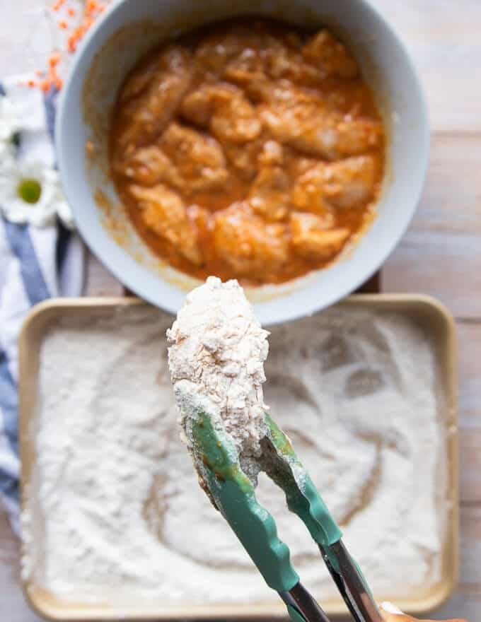 A hand holding a fully coated piece of chicken showing the final flour coating. 