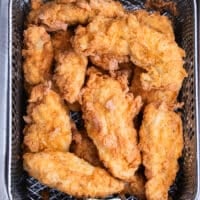 Chicken fingers removed from the hot oil and draining in the fryer basket