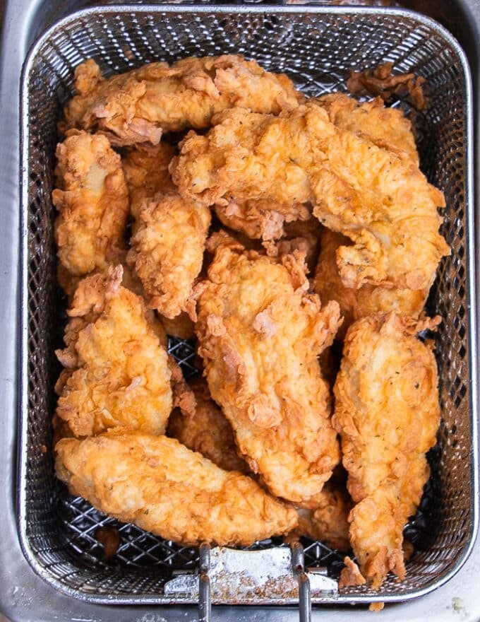 Chicken fingers removed from the hot oil and draining in the fryer basket