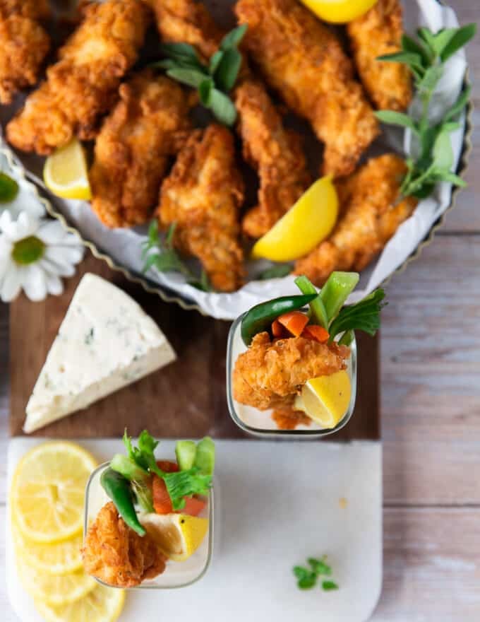 A large table with a platter of chicken fingers along side several cups of blue cheese dressing and lemon wedges 