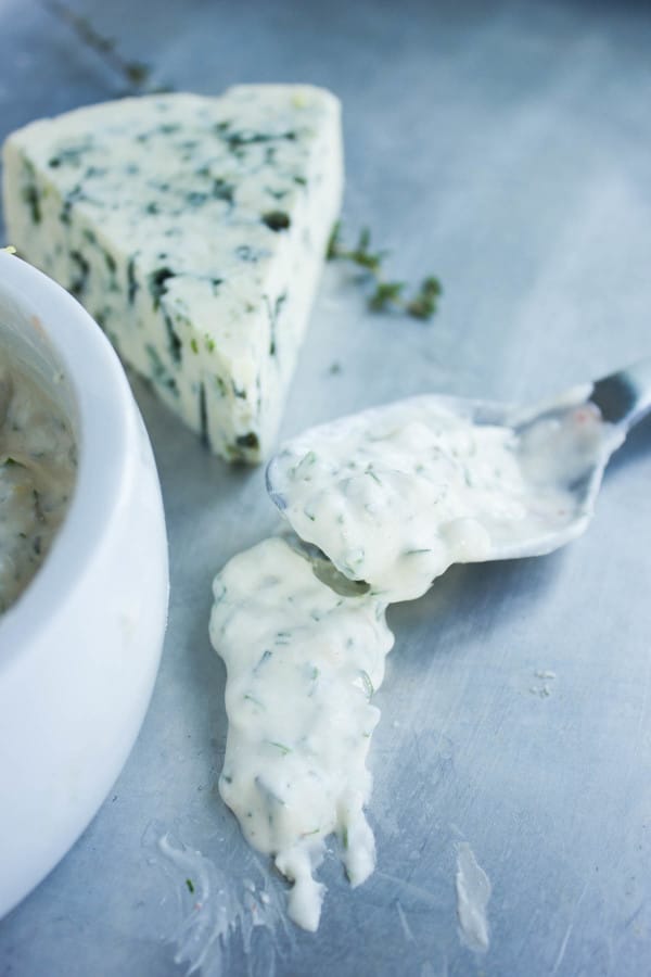 a spoon of Garlic Blue Cheese Dip on a sliver tabletop with a wedge of blue cheese in the background